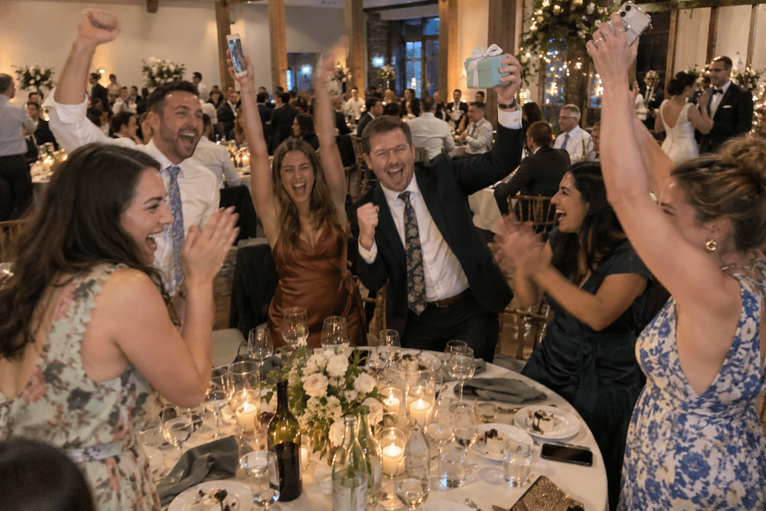 A table of friends jumping up and cheering at a reception